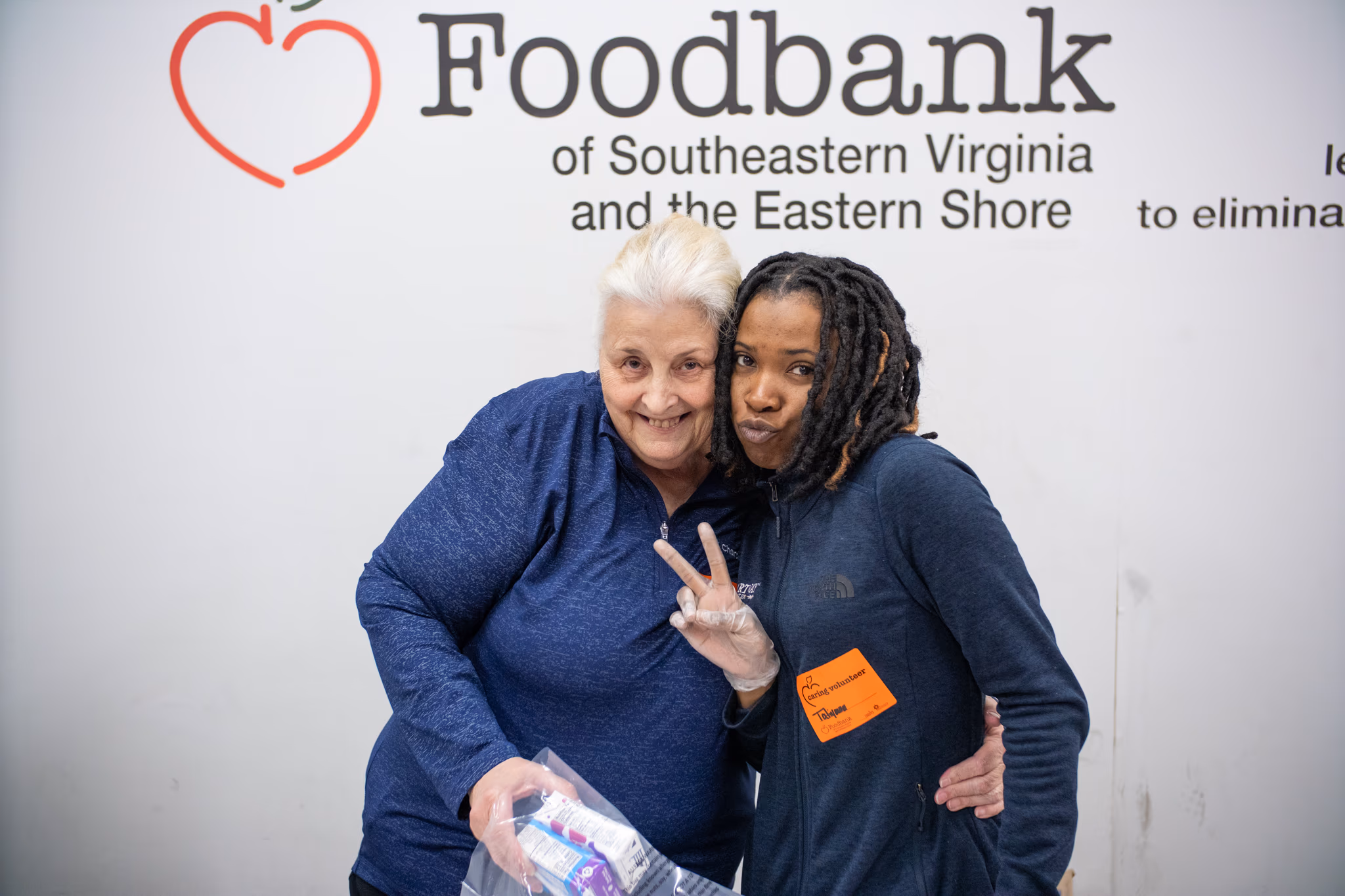 Two smiling volunteers posing together at the Foodbank of Southeastern Virginia, promoting community involvement and support for local initiatives.